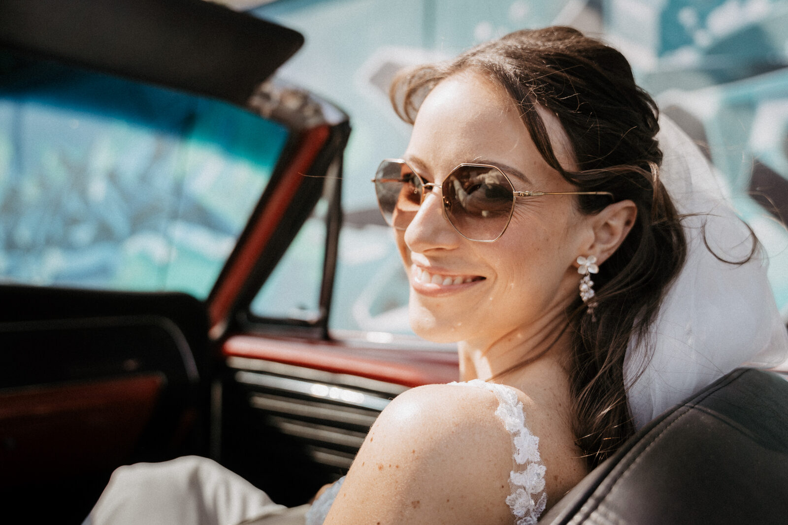 Braut mit Sonnenbrille lacht im roten Cabrio