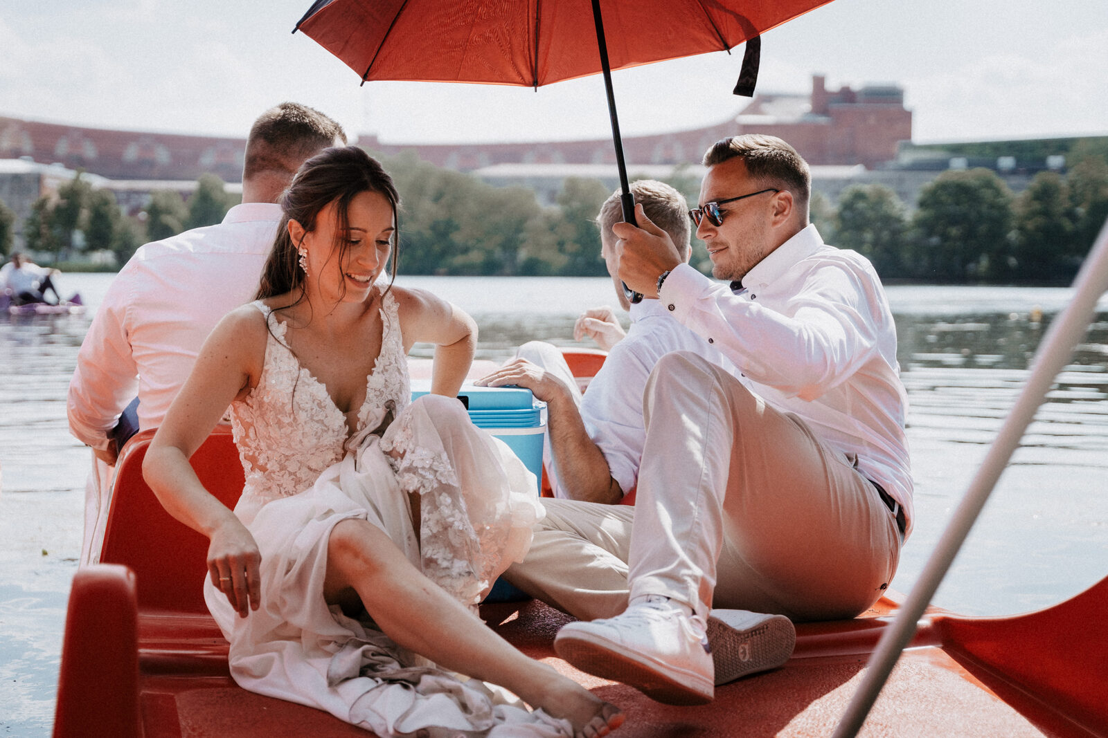 Braut im Brautkleid sitzt im Tretboot unter einem roten Schirm