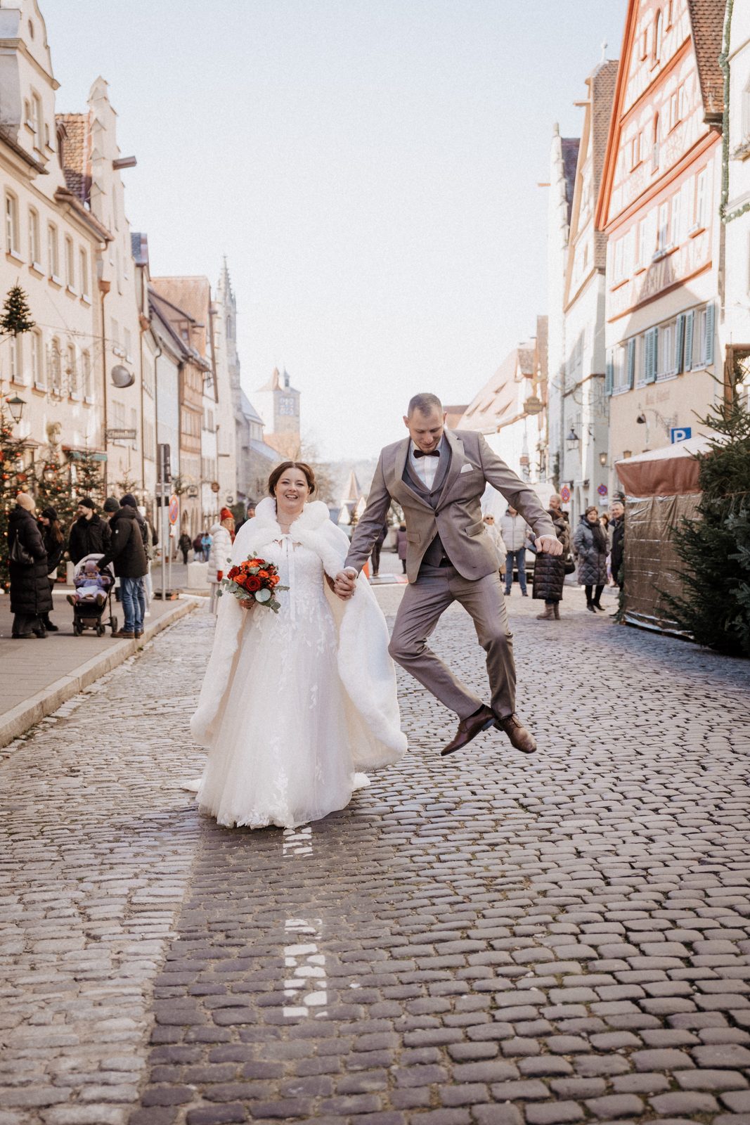 Brautpaar auf dem Kopfsteinpflaster der Rothenburger Altstadt, der Bräutigam springt vor Freude