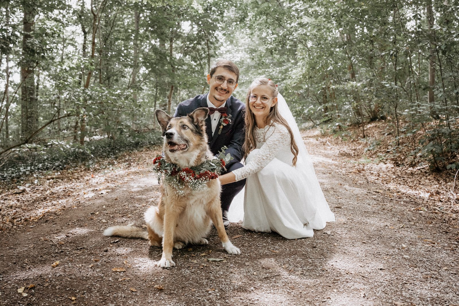 Brautpaar kniet beim First Look im Wald neben seinem Hund