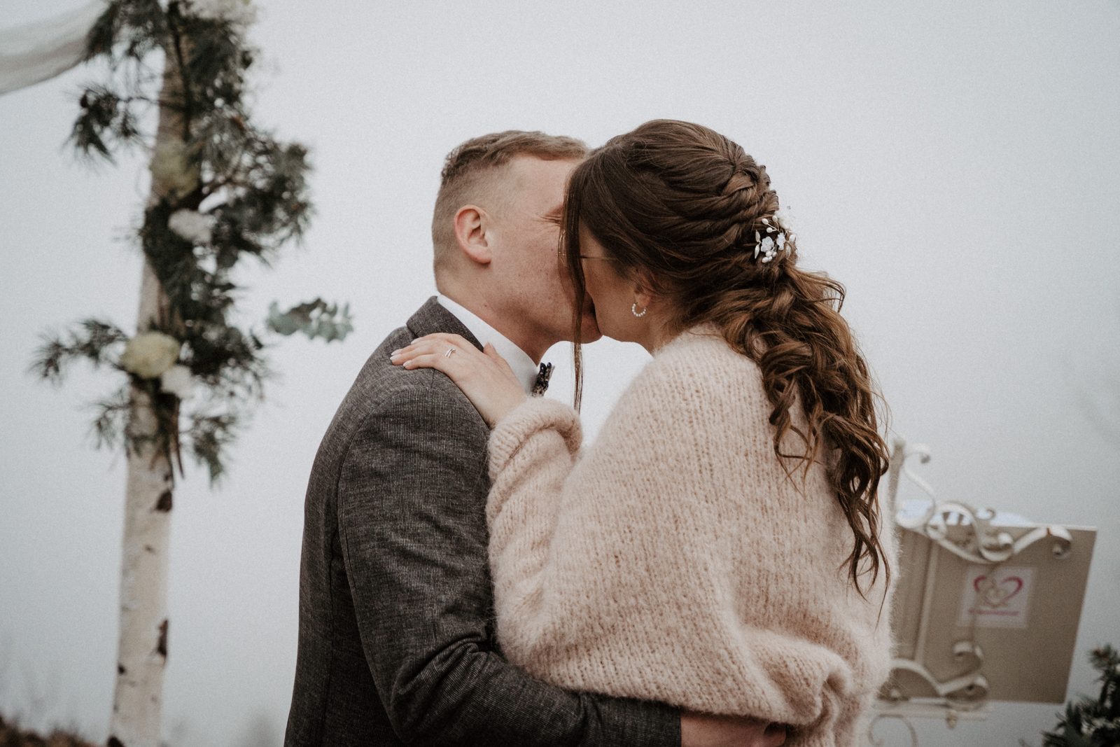 Brautpaar steht nah beieinander vor einem Blumenbogen bei einer Winterhochzeit