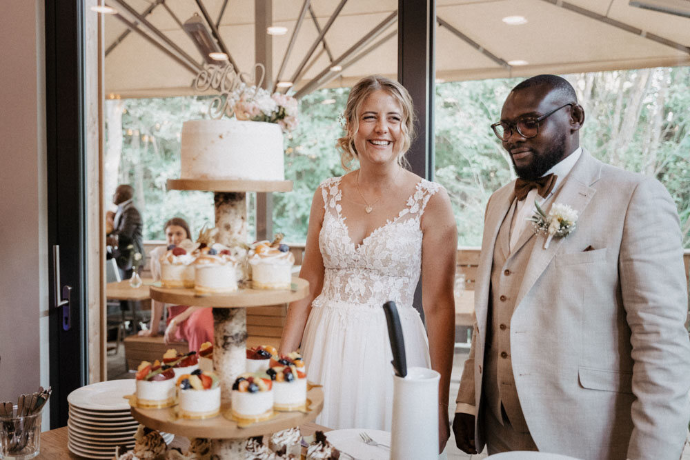 Brautpaar steht lachend vor der Hochzeitstorte und der Dessertetagere
