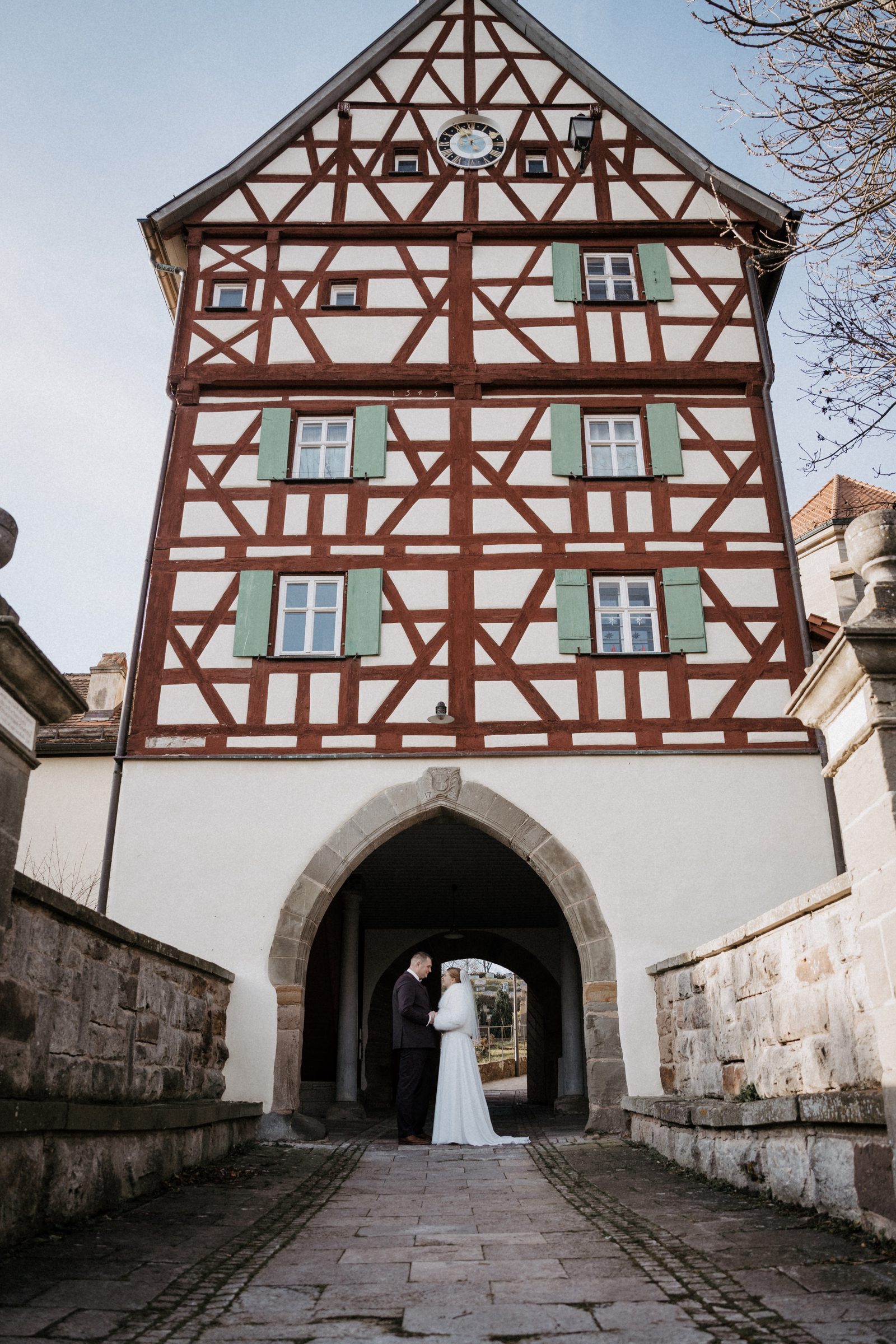 Brautpaar steht im Torbogen in Burgbernheim, dahinter führt der Gehweg hinauf zur Kirche