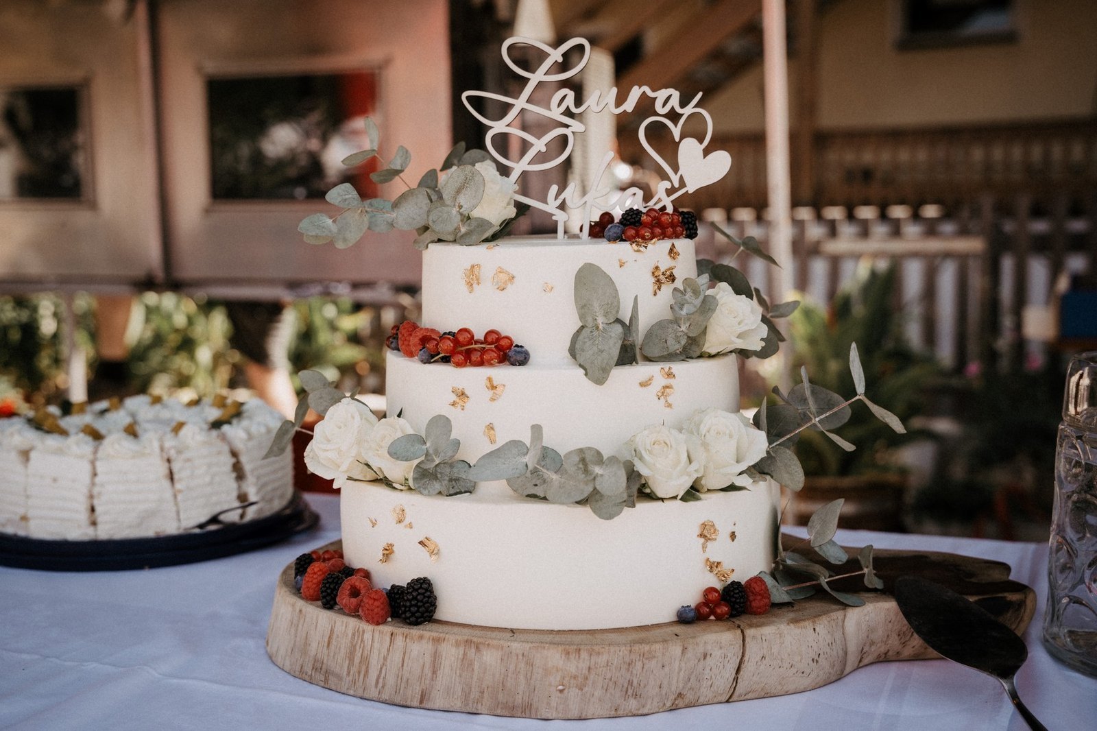 Zweistoeckige Hochzeitstorte mit Eukalyptus und Beeren auf einer Holzscheibe