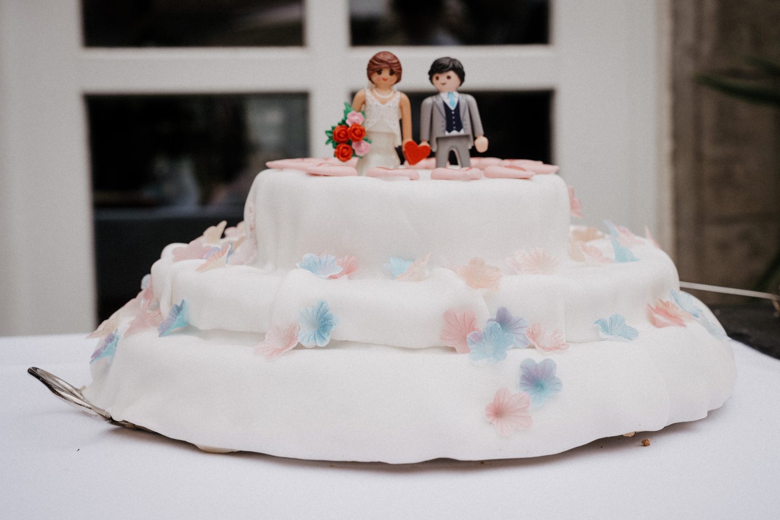 Dreistöckige Hochzeitstorte mit Blüten und zwei Figuren obenauf