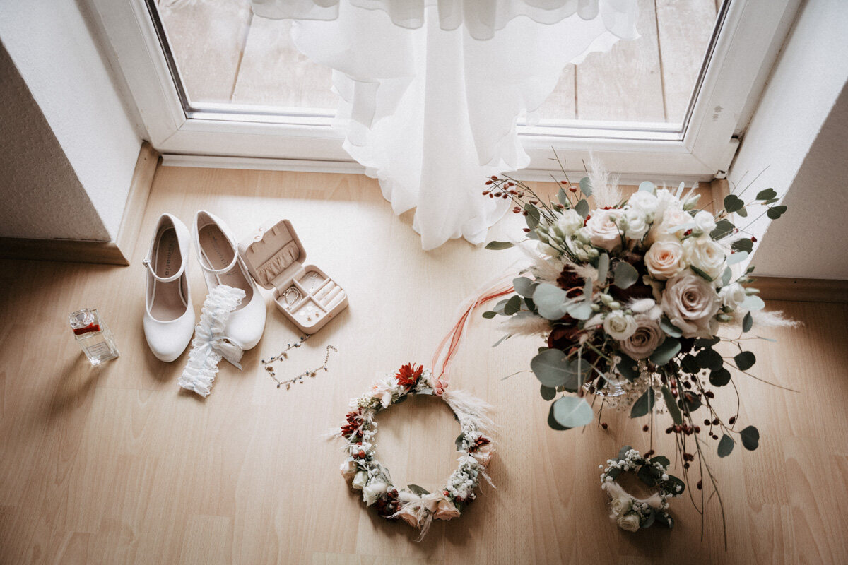 Brautschuhe, Blumenkranz und Brautstrauß liegen im Licht am Fenster