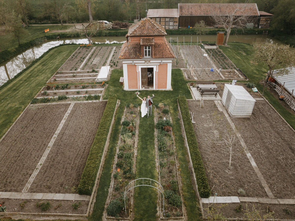 Luftaufnahme des roten Wasserschlösschens zwischen Gartenbeeten