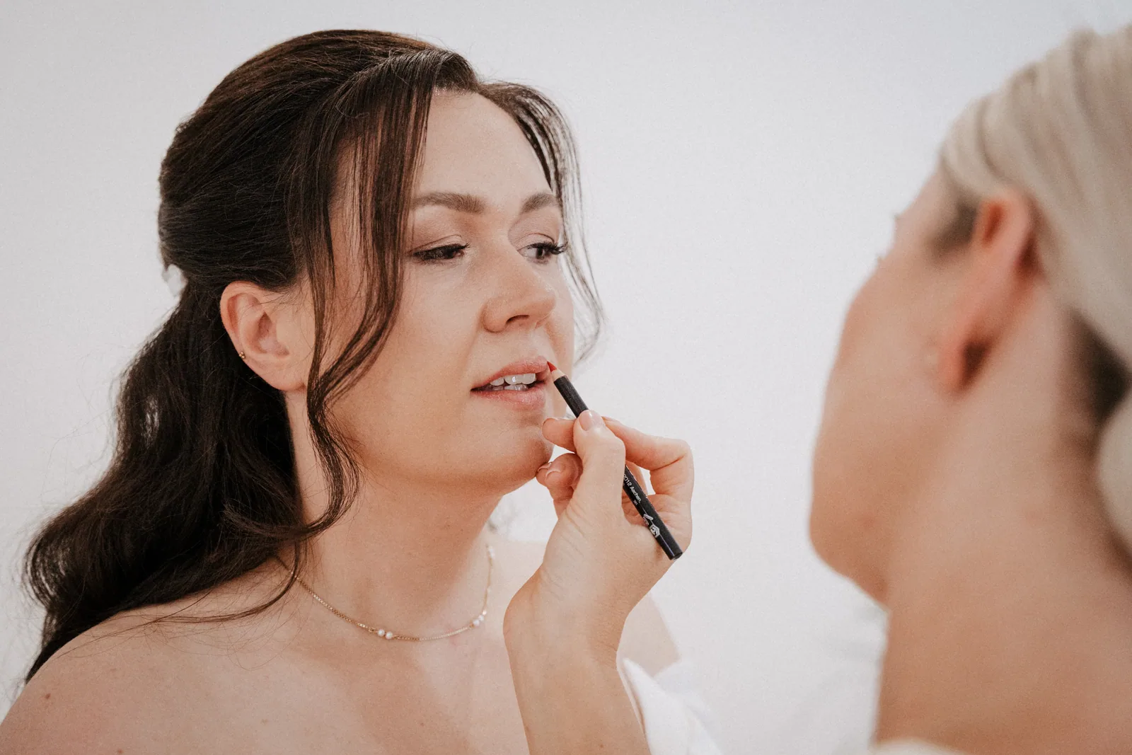 Braut beim Schminken, die Stylistin trägt Lippenstift auf