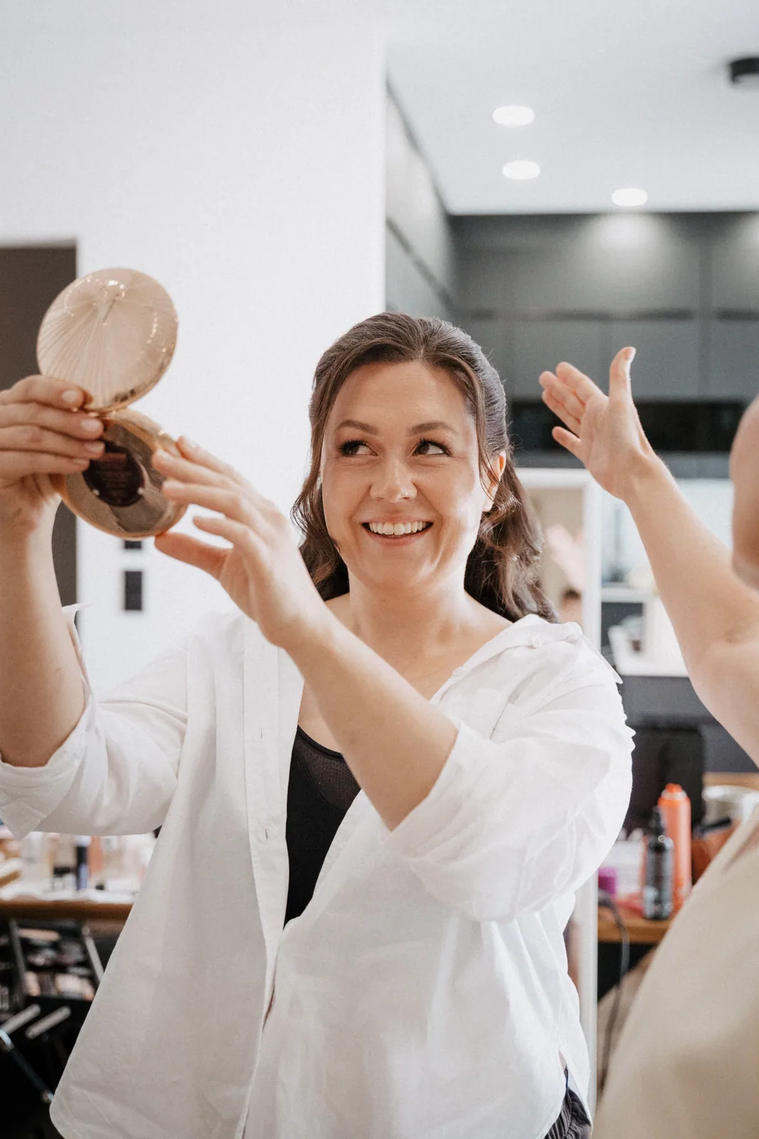 Braut lacht beim Getting Ready und hält einen Handspiegel hoch