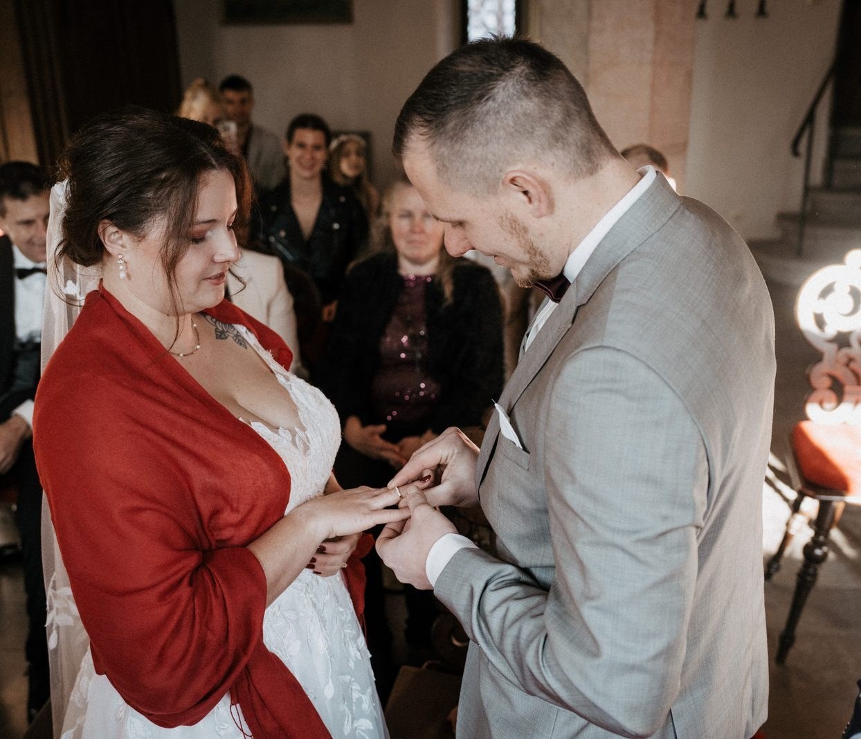 Der Bräutigam steckt der Braut den Ring an, im Hintergrund die Gäste im Trauzimmer
