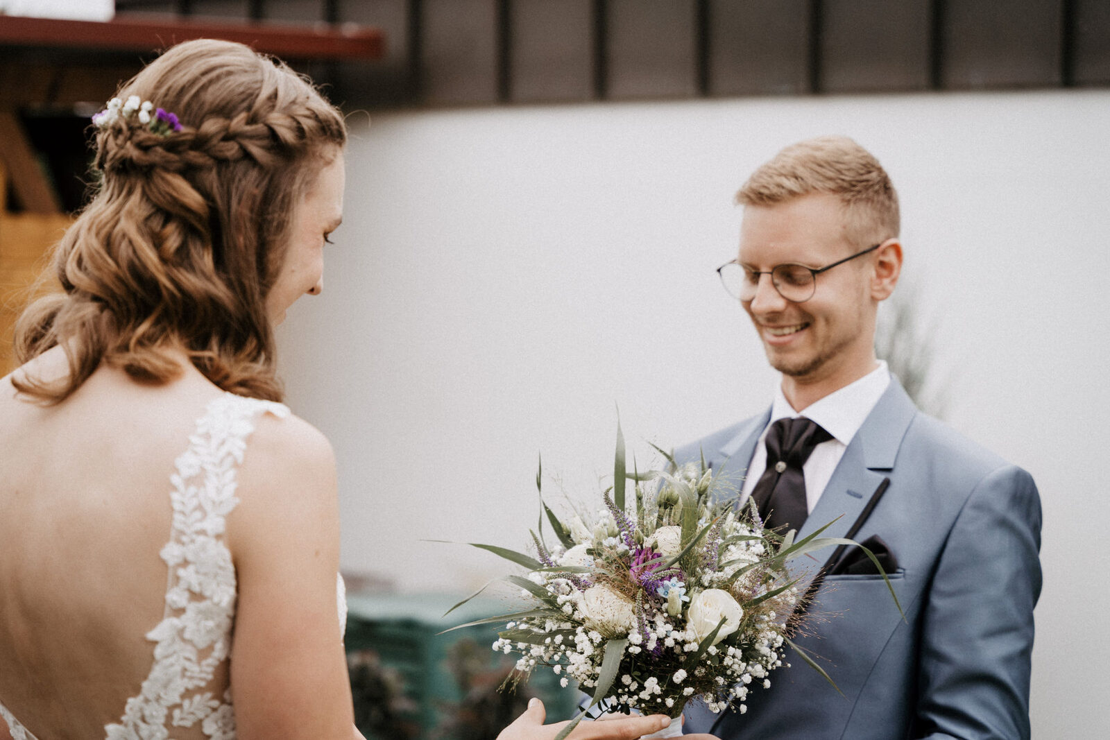 Braut überreicht ihrem Bräutigam beim First Look im Garten den Brautstrauß