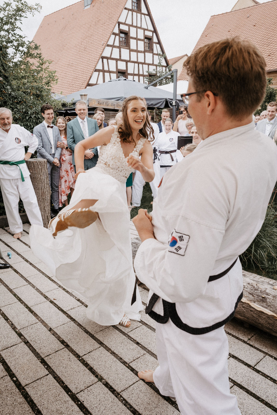 Braut tritt im Brautkleid ein Brett, das ein Taekwondo-Sportler hält