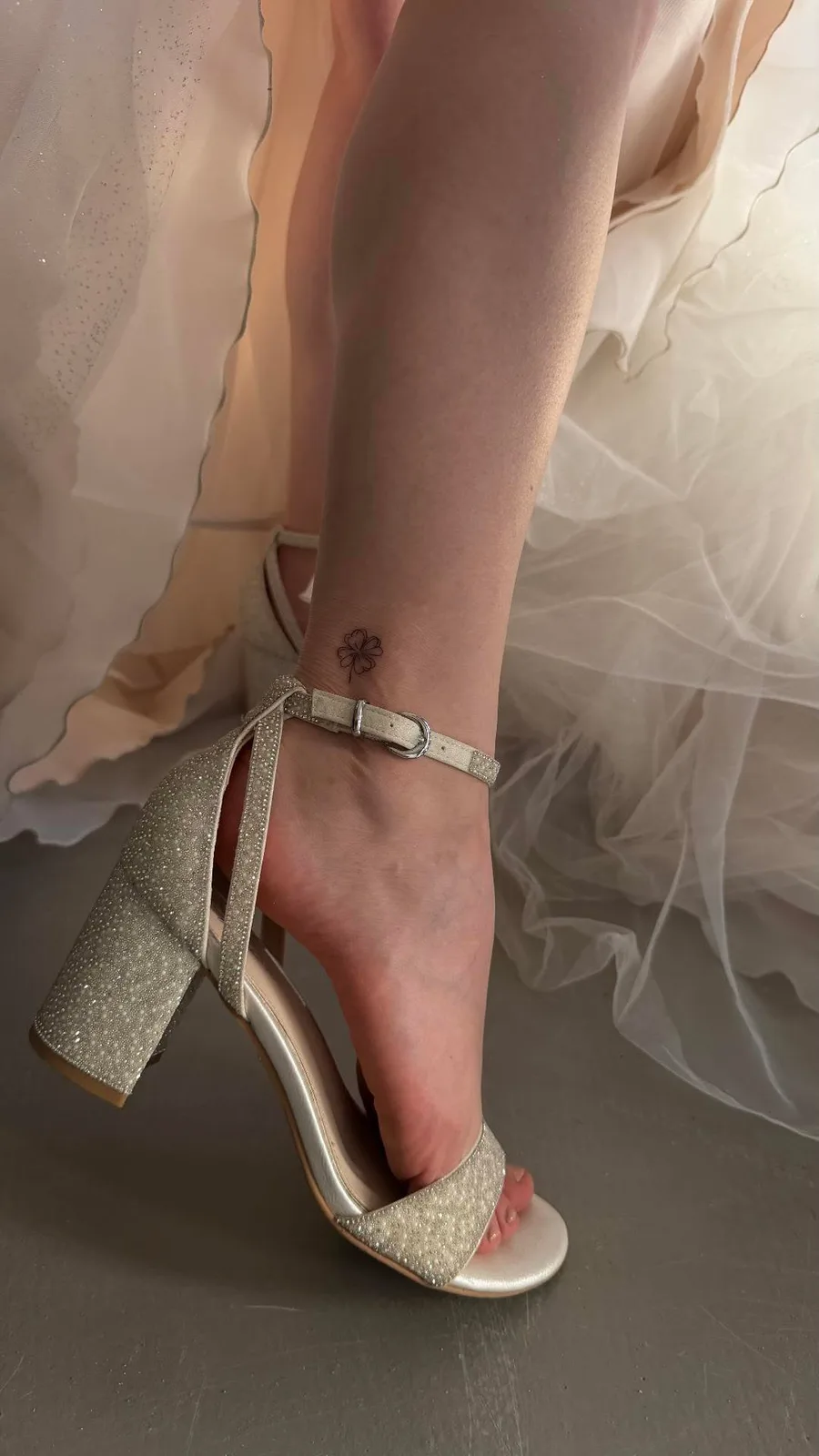 Mini-Tattoo auf der Hochzeit, frisch gestochen an der Ferse neben einem glitzernden Brautschuh