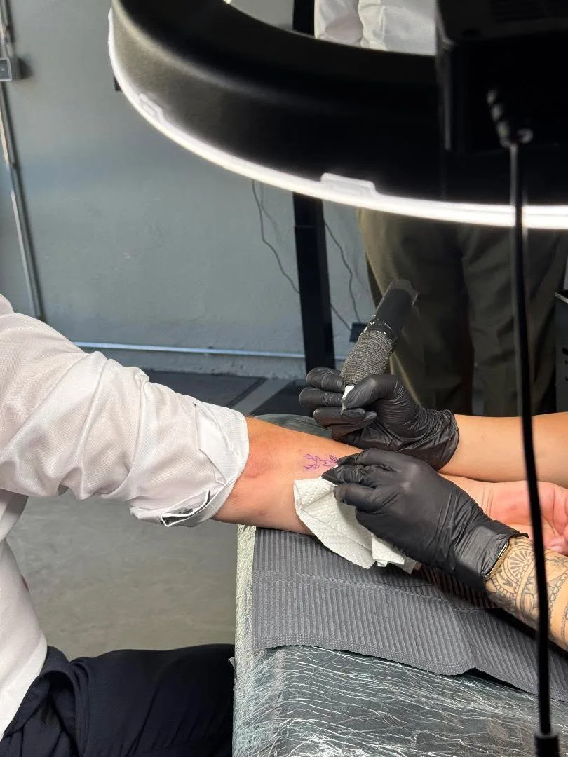 Tattoo auf der Hochzeit, Jessi sticht unter der Arbeitslampe ein feines Motiv auf einen Unterarm