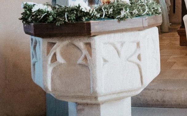 Steinernes Taufbecken mit Grün und weißen Blüten in einer Dorfkirche in Franken