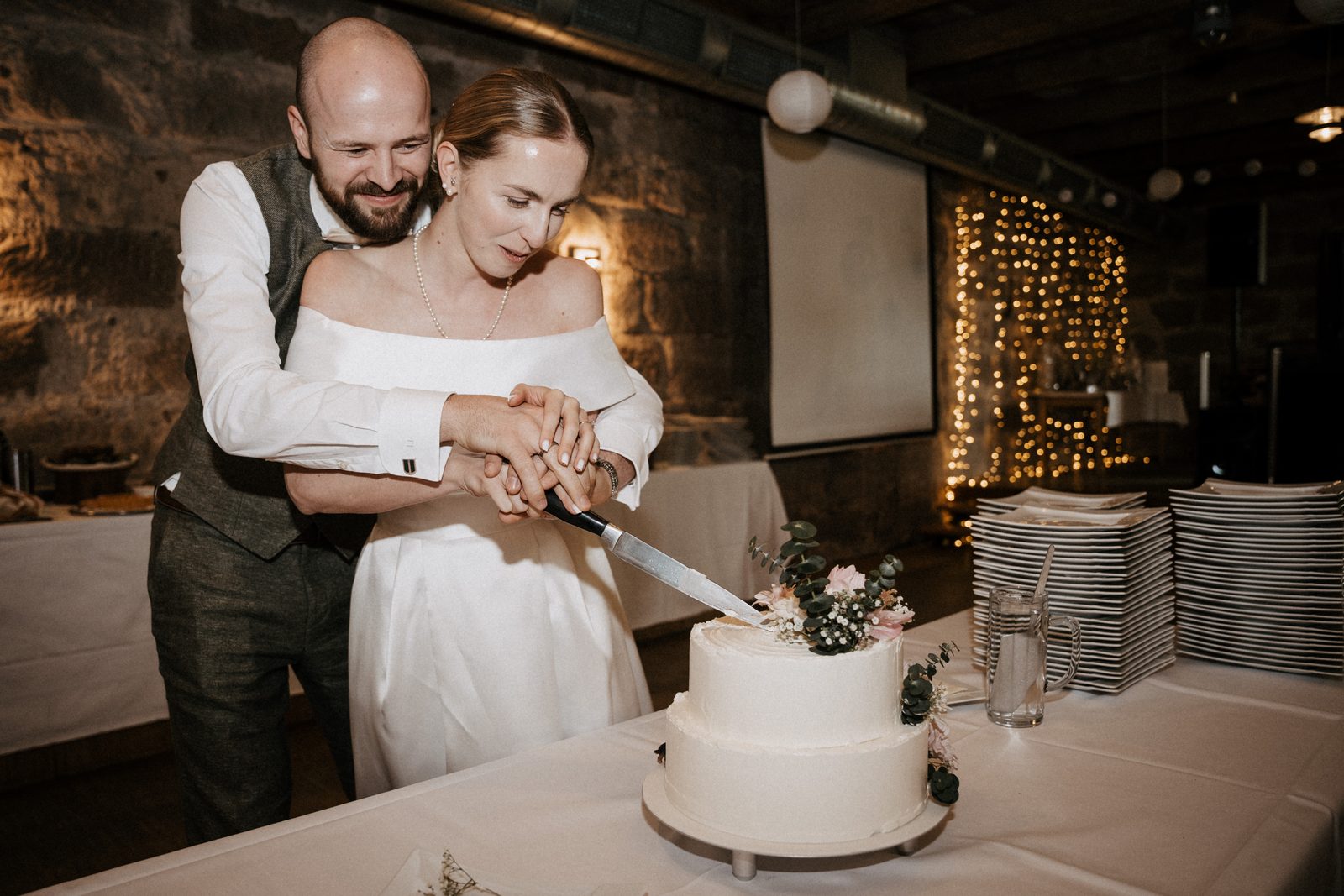Brautpaar schneidet die Hochzeitstorte vor der alten Sandsteinwand der Festscheune im Bauhof Cadolzburg an