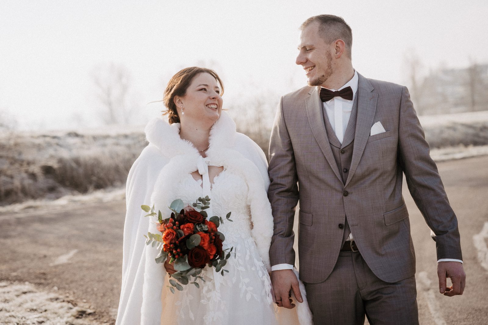 Brautpaar lacht im Raureif bei einer Winterhochzeit in Rothenburg ob der Tauber, die Braut mit rotem Brautstrauß und weißer Stola