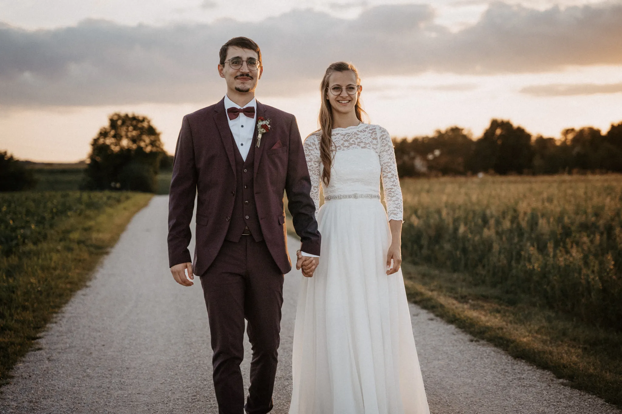 Brautpaar geht im Abendlicht einen Feldweg entlang, Hochzeitsfotografie in Franken