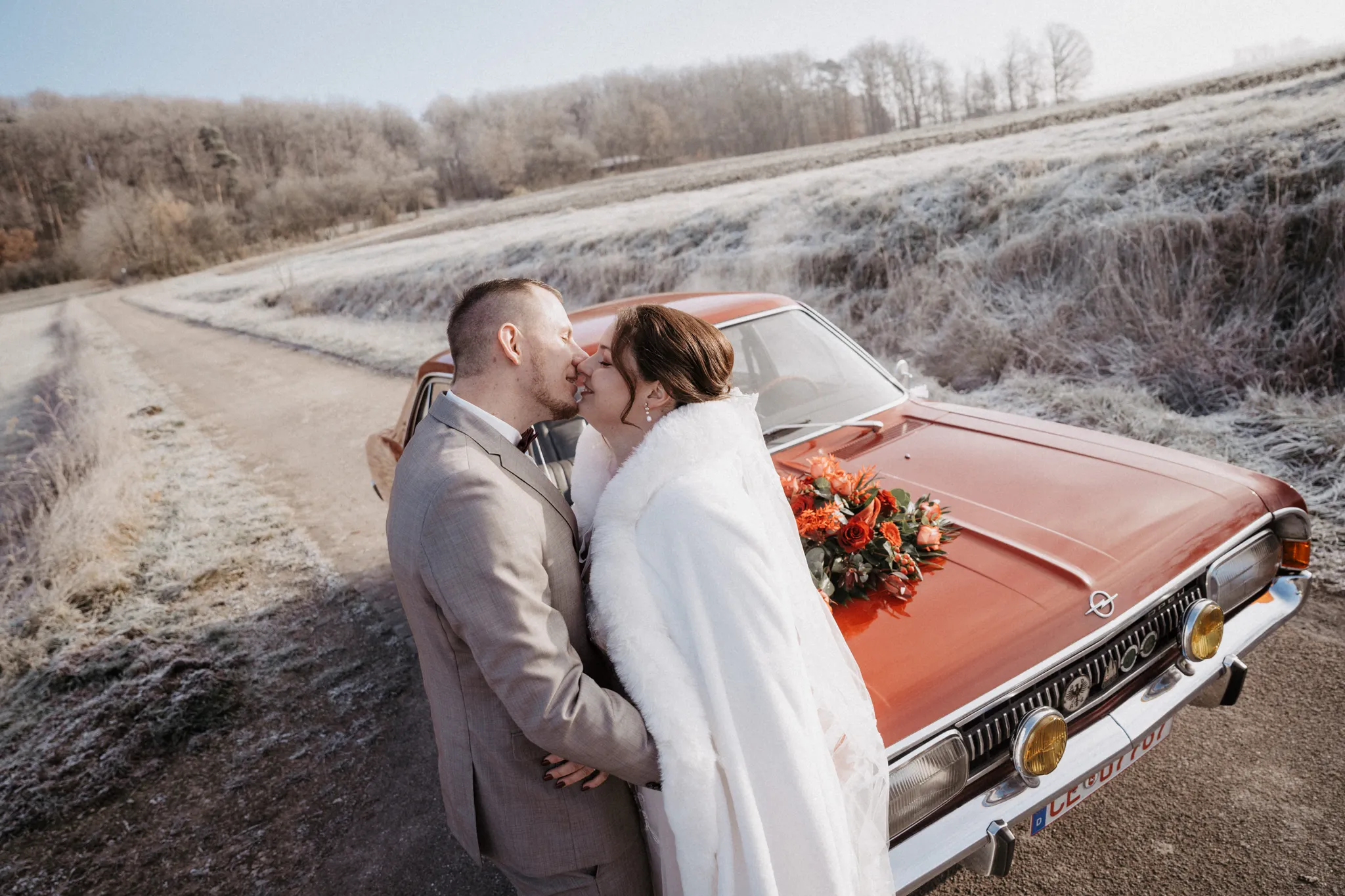 Brautpaar küsst sich vor dem roten Oldtimer bei einer Winterhochzeit bei Rothenburg
