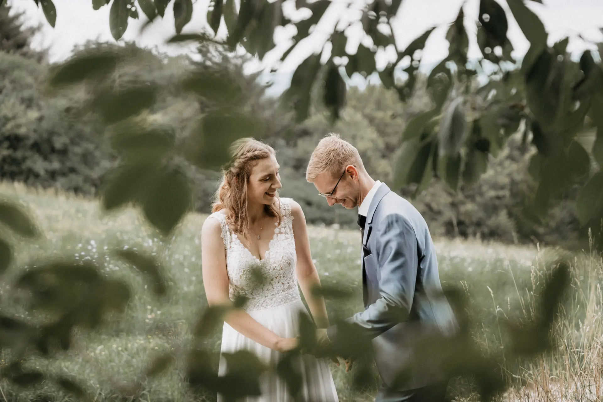 Ein Brautpaar steht zusammen im Freien, lächelt und umgeben von Bäumen, der perfekte Moment eingefangen durch die Linse eines Hochzeitsfotografen