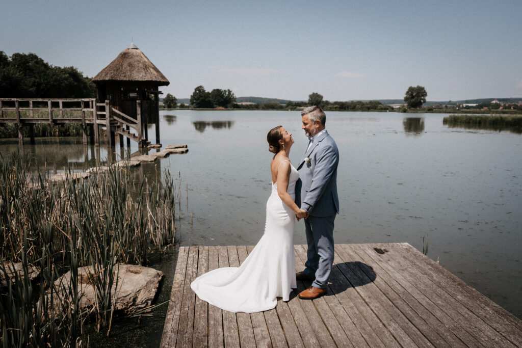 hochzeit neustadt aisch Brautpaar steht händehaltend auf Steg am Uehlfeld See