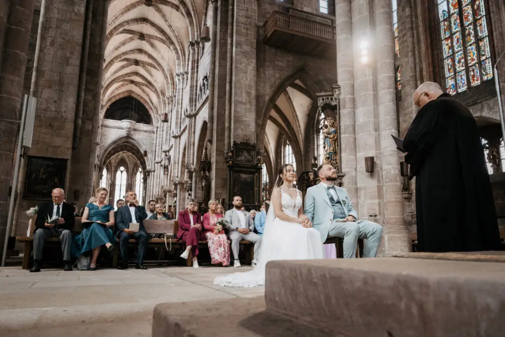 Braut und Bräutigam sitzen auf Stühlen bei kirchlicher Trauung, imposante Alstadtkirche Nürnberg im Hintergrund